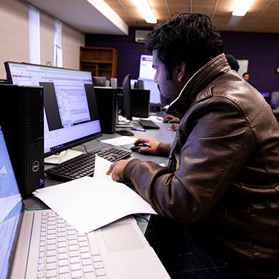 a student working at a computer while looking through papers