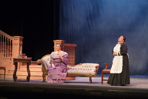 Two women in a living room. One is seated on a couch.