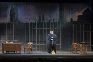 A man stands in front of a prison cell with a broom.