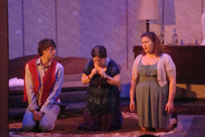 Three people kneeling, one woman has her head bowed.