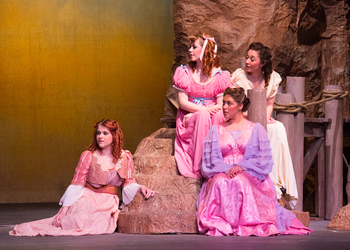 Four women seated in fancy dresses look off camera.