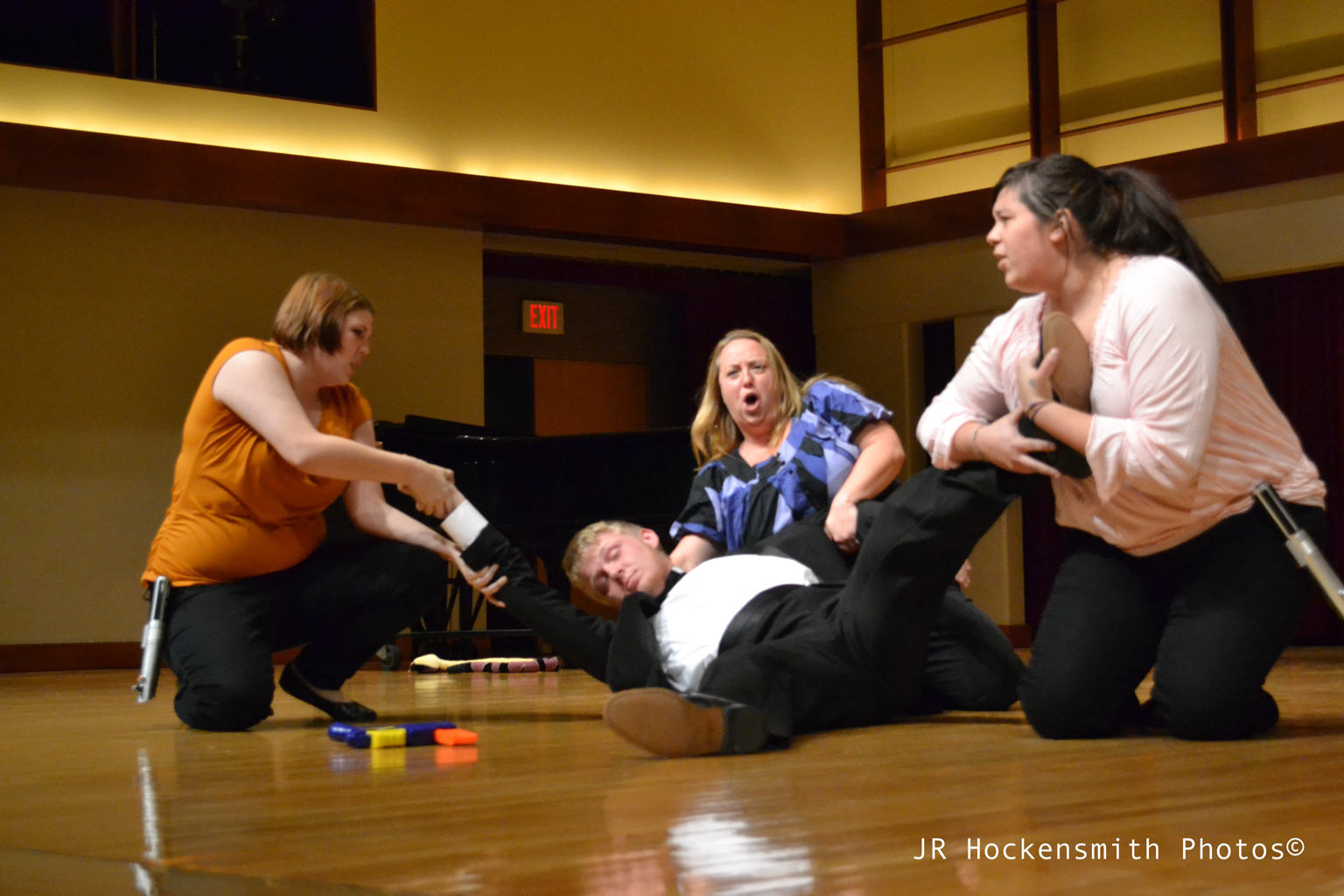 Three women tug at the limbs of a man lying on the ground.