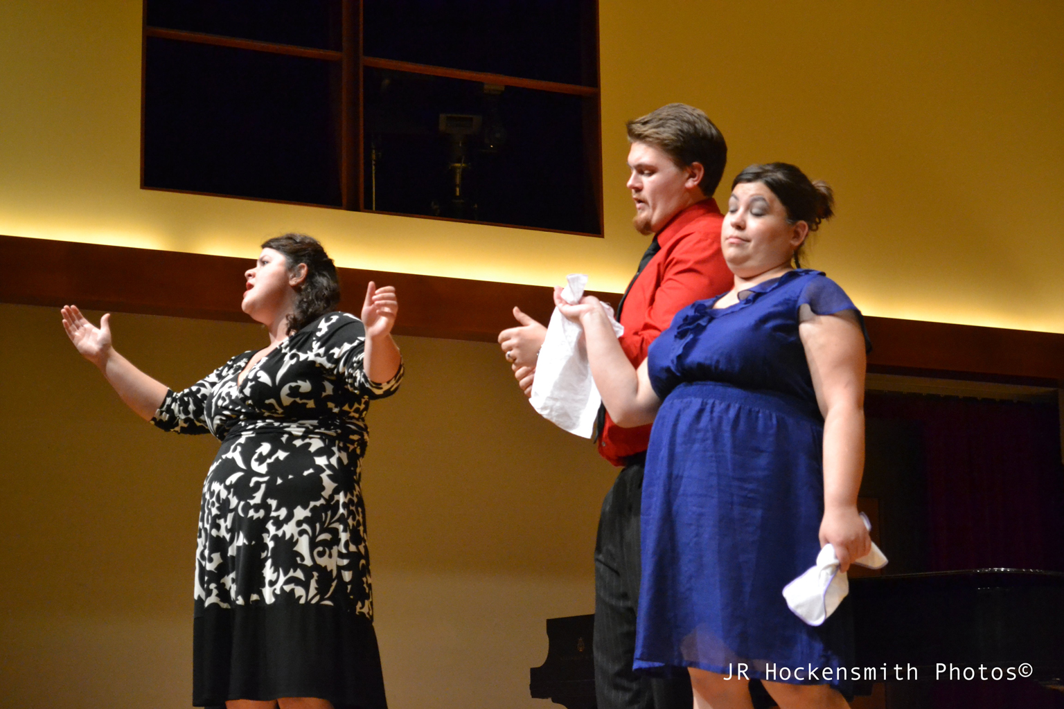 A woman sings while a man and a woman stand by.