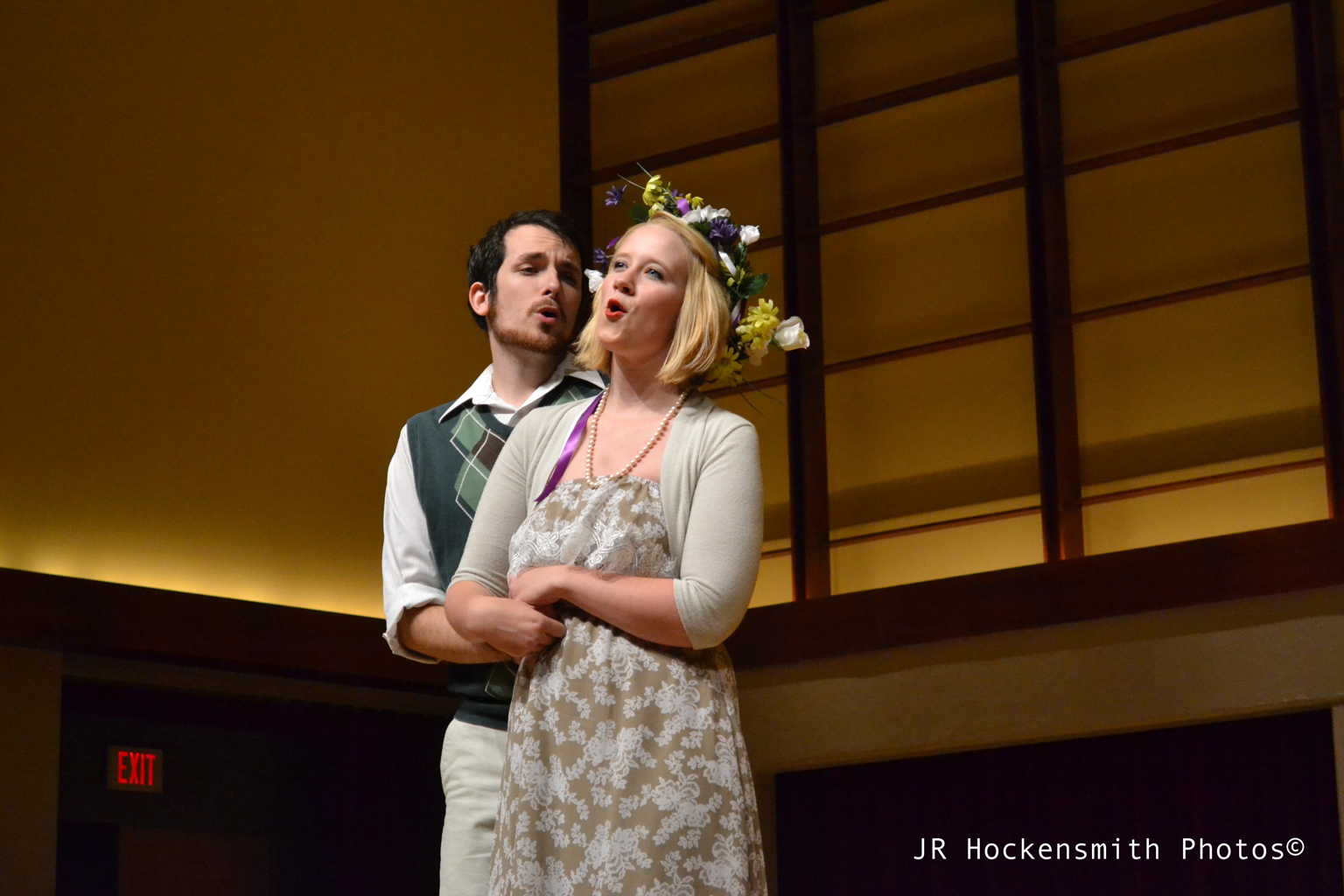 A man holds a woman in his arms while singing a duet.