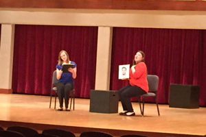 Two women sing while holding portraits of men.