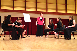 Two women sing while holding portraits of men.